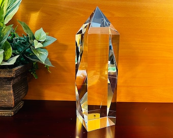 May include: A clear glass crystal prism with a pointed top and a rectangular base. The prism is sitting on a wooden surface.