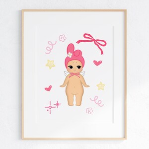 May include: A framed print featuring a whimsical illustration of a cherubic figure. The figure is depicted with a pink bonnet, small wings, and a bow. Pink hearts, stars, and decorative swirls surround the figure, creating a playful and charming aesthetic.