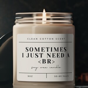 May include: A lit soy wax candle in a clear glass jar with a black lid. The label reads "Clean Cotton Scent" and "Sometimes I Just Need a <BR>". The candle is 9 oz and has a burn time of 50-60 hours. The background is dark.