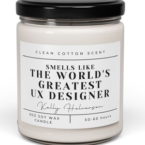 May include: A white soy wax candle in a clear glass jar with a black lid. The label reads "CLEAN COTTON SCENT" and "SMELLS LIKE THE WORLD'S GREATEST UX DESIGNER" with a name and burn time.