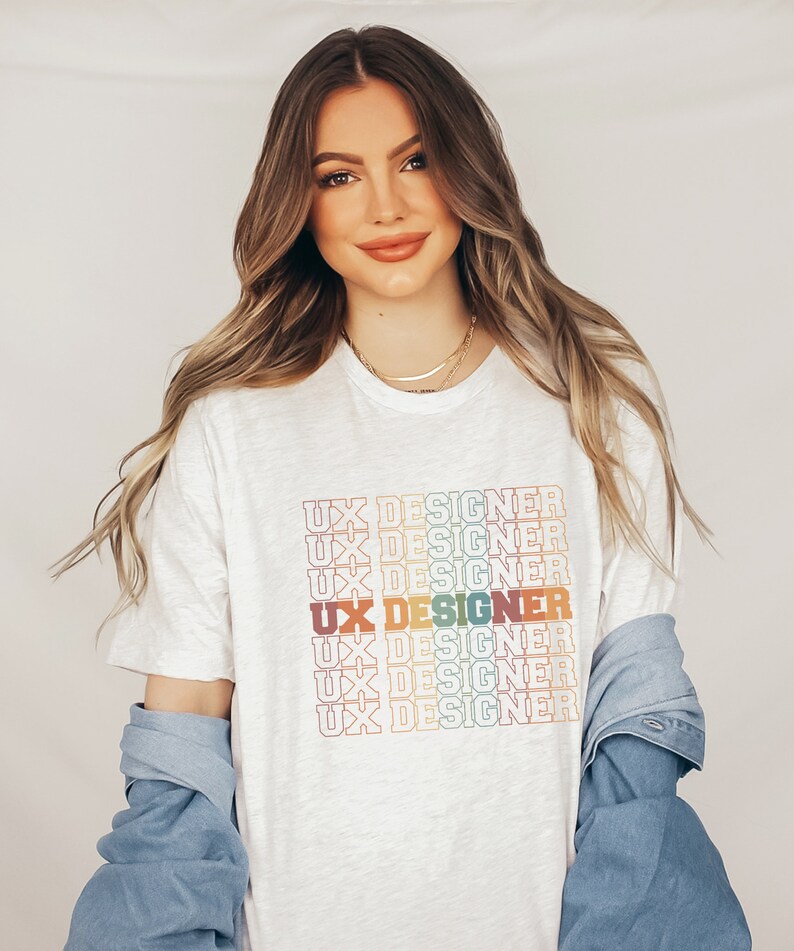 May include: A white t-shirt with the text "UX Designer" repeated in a rainbow color pattern.