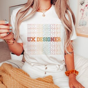 May include: White t-shirt with the text "UX DESIGNER" repeated in a rainbow color pattern.