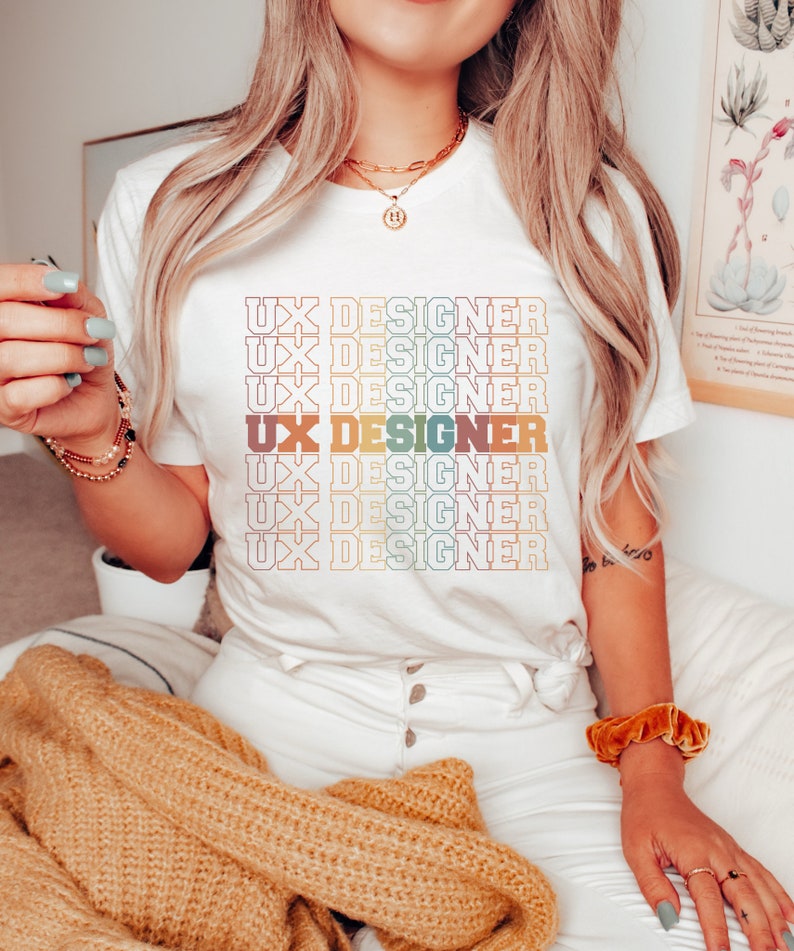 May include: White t-shirt with the text "UX DESIGNER" repeated in a rainbow color pattern.