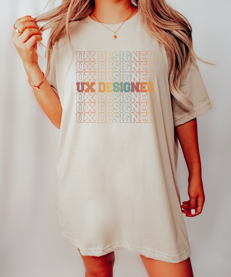 May include: A beige oversized t-shirt with the text "UX Designer" repeated in a rainbow pattern.
