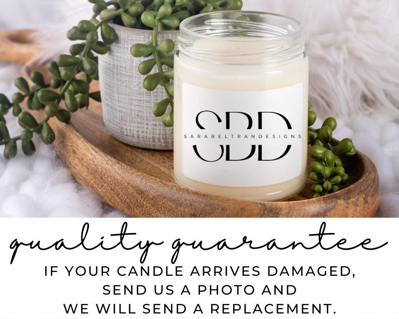 May include: A white candle in a glass jar with a white label that says "CDD SARABELTRANDESIGNS UDD". The candle is sitting on a wooden tray with green plants.