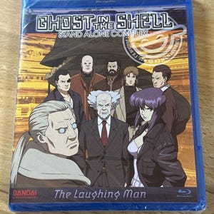 May include: A blue Blu-ray disc case for "Ghost in the Shell: Stand Alone Complex - The Laughing Man." The cover features a group of anime characters and the series title in bold white letters.