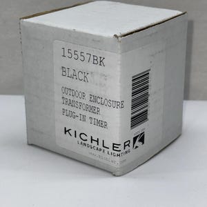 May include: A white cardboard box for a Kichler landscape lighting outdoor enclosure transformer plug-in timer, model 15557BK. The label features the brand name, product description, a barcode, and the website address printed in black text.
