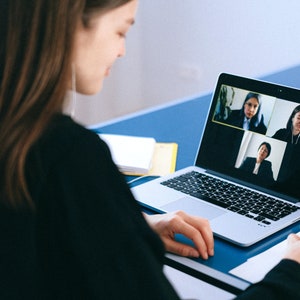 Puede incluir: Una persona está en una videollamada con otras tres personas en una computadora portátil. La persona está tomando notas en un papel.