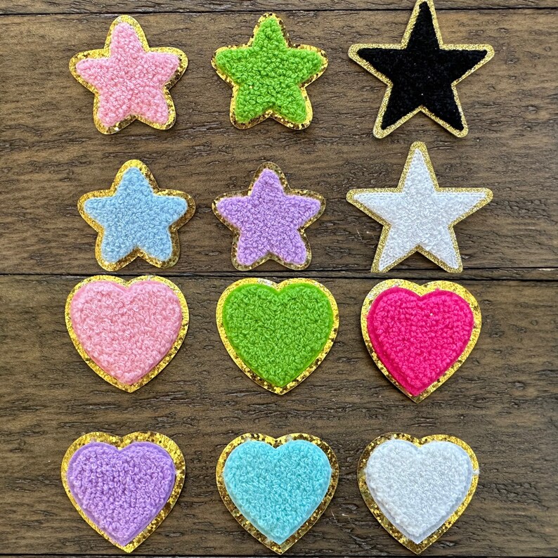 May include: Twelve iron-on patches in various colors and shapes, including stars and hearts. The patches are made of fuzzy fabric and have a gold outline.