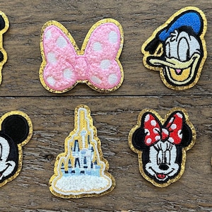 May include: Ten embroidered iron-on patches featuring various Disney characters, including Mickey Mouse, Minnie Mouse, Donald Duck, Goofy, and Pluto. The patches are all gold-trimmed and have a variety of colors and designs.
