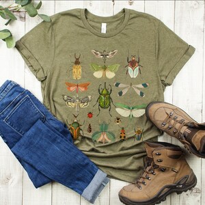 May include: A green t-shirt with a vintage illustration of various insects, including beetles, butterflies, and dragonflies. The shirt is paired with blue jeans and brown hiking boots.