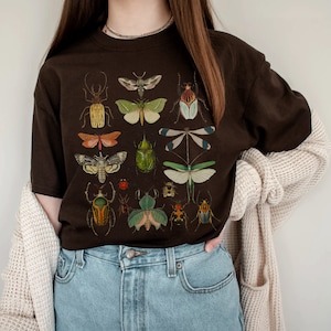 May include: A brown t-shirt with a graphic print of various insects and butterflies. The insects are depicted in a vintage style with intricate details and vibrant colors.