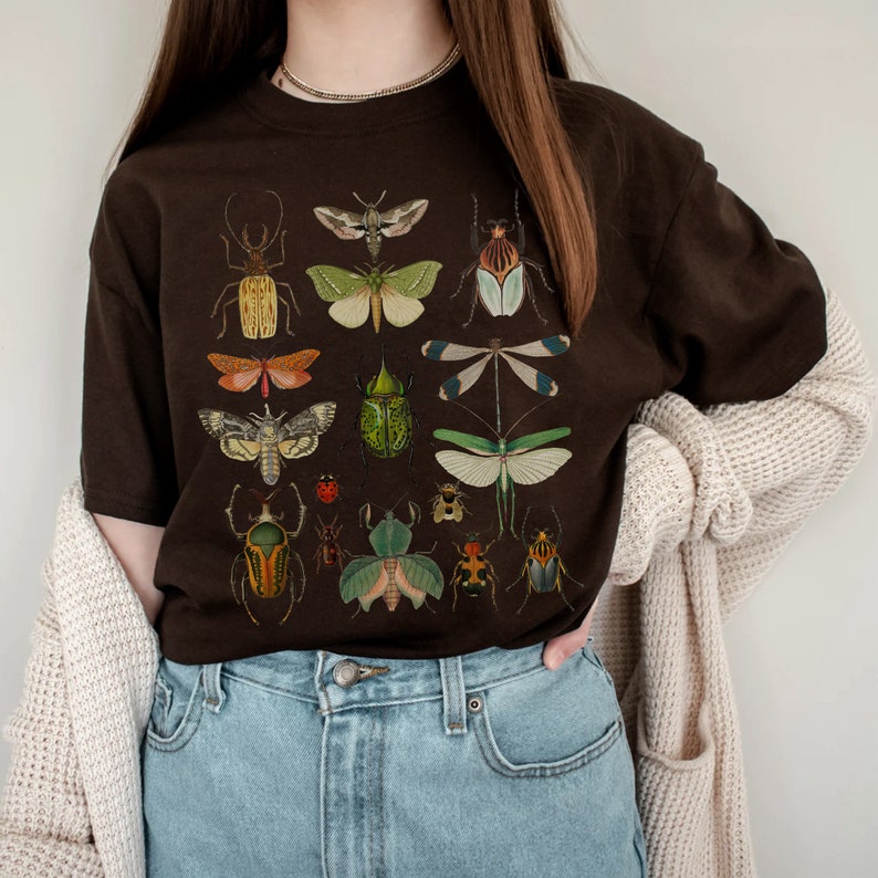 May include: A brown t-shirt with a graphic print of various insects and butterflies. The insects are depicted in a vintage style with intricate details and vibrant colors.