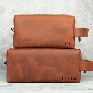 Pu&ograve; includere: Due trousse da toilette in pelle marrone con le iniziali "CA" e "TYLER" incise.