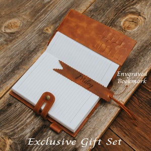 May include: A brown leather journal with a matching leather bookmark. The bookmark is engraved with the name "Miley". The journal has a flap closure and a pen loop. The journal and bookmark are part of an "Exclusive Gift Set".