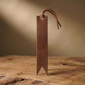 May include: A brown leather bookmark with a decorative cut at the bottom and a loop at the top. The bookmark has the text "Your smile paints colours on my world and your touch ignites my soul" engraved on it.