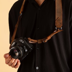 May include: A brown leather camera strap with a metal buckle and a Canon EOS 5D camera attached.