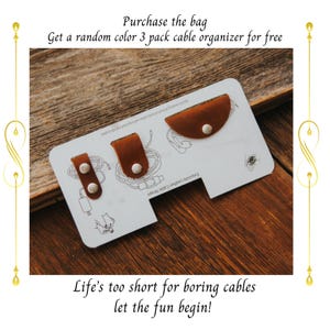 Pu&ograve; includere: Un cartoncino bianco con la scritta "Exquisite Leather Cable Straps" e tre organizzatori di cavi in ​​cuoio marrone con bottoni bianchi. Il cartoncino &egrave; su una superficie di legno. Il testo "Purchase the bag Get a random color 3 pack cable organizer for free" &egrave; nella parte superiore dell'immagine. Il testo "Life's too short for boring cables let the fun begin!" &egrave; nella parte inferiore dell'immagine.