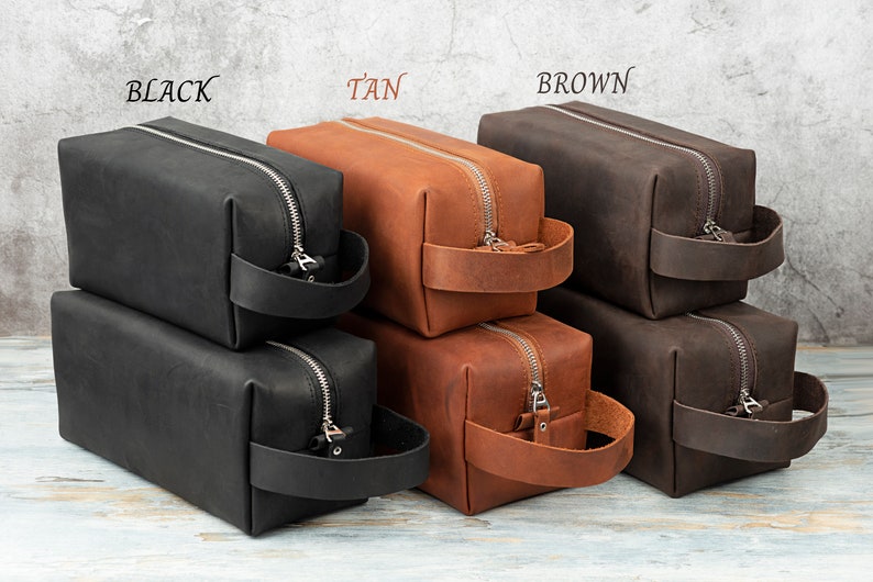 Pu&ograve; includere: Tre pile di pochette da toilette in pelle nera, marrone chiaro e marrone. Ogni pochette ha una chiusura a zip e un manico in pelle.