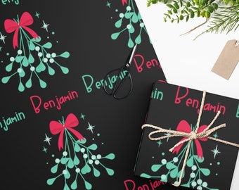 Puede incluir: Papel de regalo negro con un patrón repetido de ramitas de muérdago verdes con lazos rojos y el nombre "Benjamin" en letras rosas.