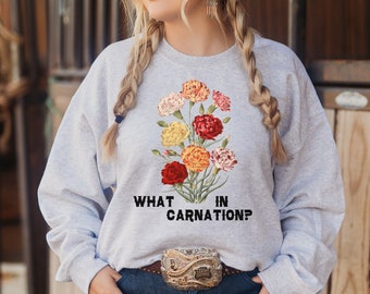 Peut inclure: Un sweat-shirt gris avec un motif floral et le texte "WHAT IN CARNATION?" imprimé sur le devant.