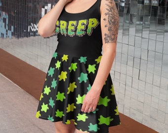 Op de afbeelding: Zwarte skaterjurk met een groene en gele slijmprint en het woord "CREEP" in druppelende letters.