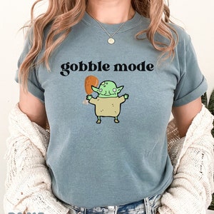 May include: A light blue t-shirt with the text "gobble mode" and a cartoon illustration of a green goblin holding a fried chicken leg.