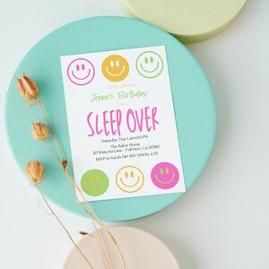 Op de afbeelding: Een witte uitnodiging met roze, groene en gele smiley's. De uitnodiging is voor een slaapfeestje om Jennas verjaardag te vieren. De tekst luidt "Come Celebrate Jenna's Birthday with a SLEEP OVER Saturday, May 1 at 6:00 PM The Baker Home 213 Wisteria Lane Fairview, Ca 247885 RSVP to Sarah 340 876-5764 by 4/25"