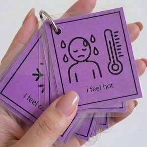 May include: A set of square purple communication cards bound by a metal ring. Each card features a black line drawing and text. One card shows a person sweating with a thermometer and the text I feel hot, while another shows a snowflake and I feel co.
