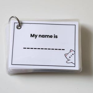 May include: A stack of white flashcards held together by a silver ring. Each card has the text "My name is" above a dashed line. A cartoon cat peeks from the bottom right corner.
