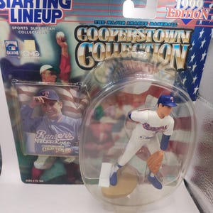 Puede incluir: Figura de la colección Cooperstown Starting Lineup de 1999 de Nolan Ryan con uniforme de los Rangers. La figura está en una funda de plástico transparente, con un respaldo estilo tarjeta de béisbol con el jugador y el logotipo del equipo.