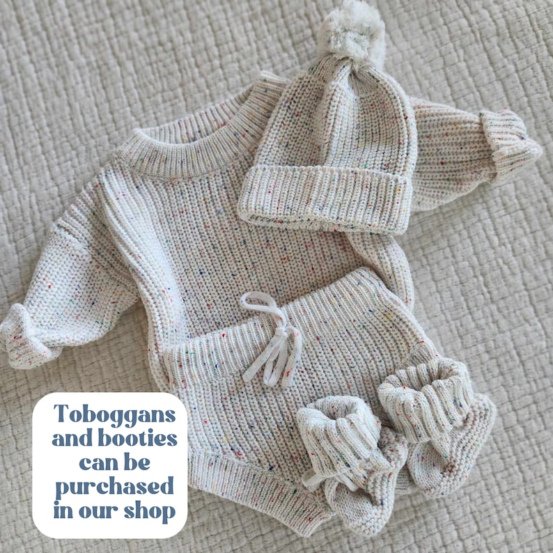May include: A cream-colored knit sweater, matching shorts with a drawstring, a beanie with a pom-pom, and two booties, all featuring a multi-colored speckled pattern. The text on the image reads: Toboggans and booties can be purchased in our shop.