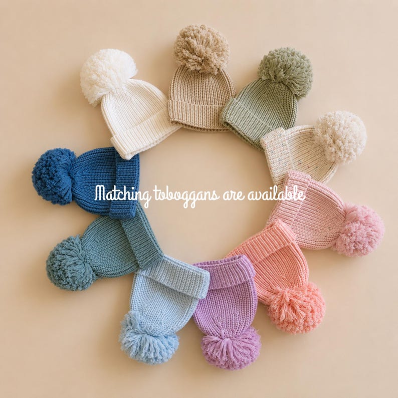 May include: A circular arrangement of ten knit beanies with pom-poms in various colors including white, beige, sage green, speckled cream, pink, lavender, light blue, teal, and dark blue. The text "Matching toboggans are available" is centered.