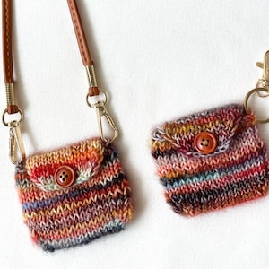 May include: Two small, hand-knitted pouches in a vibrant mix of colours, including red, orange, and purple. One has a brown leather strap with gold-tone hardware, the other has a gold-tone keychain. Each pouch features a wooden button closure.