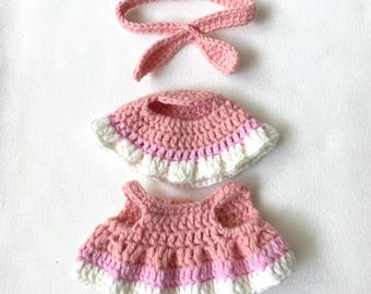 May include: A handmade crochet doll outfit in pink and white. The set includes a headband with bunny ears, a hat, and a dress. The outfit is made of soft yarn and is designed for a small doll.