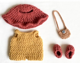 May include: A handmade crochet doll outfit set in shades of red and yellow. The set includes a hat, top, purse, and shoes. The hat and shoes are a reddish-brown color, the top is yellow, and the purse is tan with a blue button.