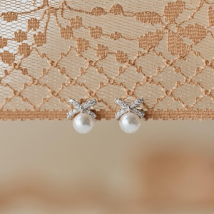 Puede incluir: Un par de pendientes de perlas con dise&ntilde;o de lazo. Los lazos est&aacute;n incrustados con peque&ntilde;os cristales brillantes. Los pendientes tienen un estilo cl&aacute;sico y elegante, perfectos para ocasiones especiales.