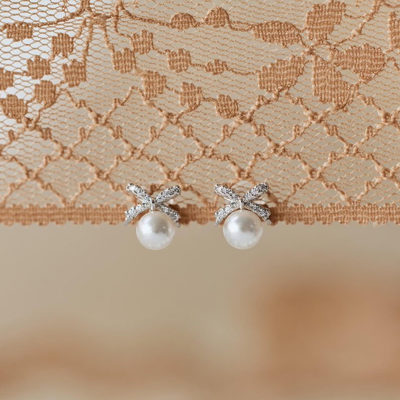 Puede incluir: Un par de pendientes de perlas con dise&ntilde;o de lazo. Los lazos est&aacute;n incrustados con peque&ntilde;os cristales brillantes. Los pendientes tienen un estilo cl&aacute;sico y elegante, perfectos para ocasiones especiales.