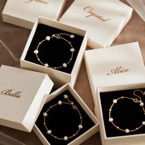 May include: Three gold-tone chain bracelets featuring small white pearls and gold beads, each presented in an individual cream-coloured square gift box. The lids are inscribed with the names Grace, Crystal, Alice, and Bella in elegant brown script.
