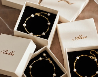May include: Three gold-tone chain bracelets featuring small white pearls and gold beads, each presented in an individual cream-colored square gift box. The lids are inscribed with the names Grace, Crystal, Alice, and Bella in elegant brown script.