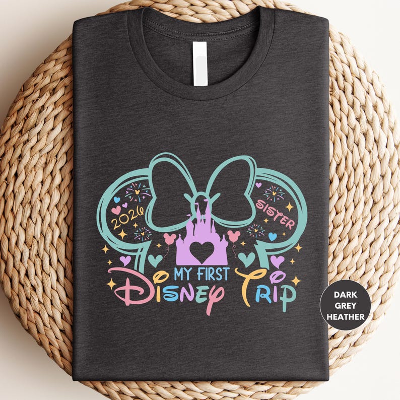 A black t-shirt with a colorful graphic design featuring a castle, Mickey Mouse ears, and the text "My first Disney trip" and "Sister" written on it.