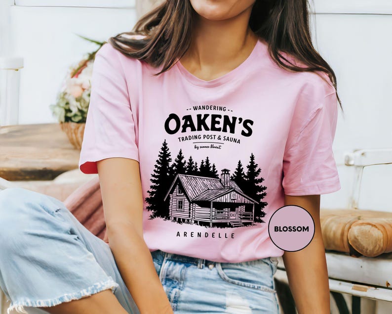 a woman wearing a pink shirt with a picture of a cabin on it