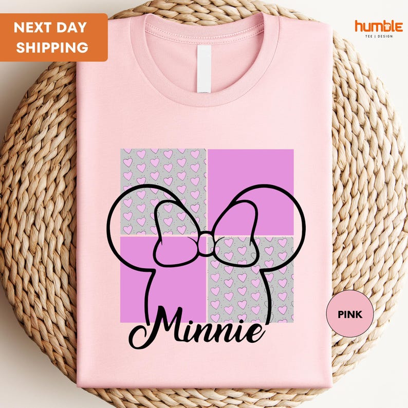 A pink t-shirt with a graphic design featuring Minnie Mouse's ears and bow, along with a pink heart pattern.