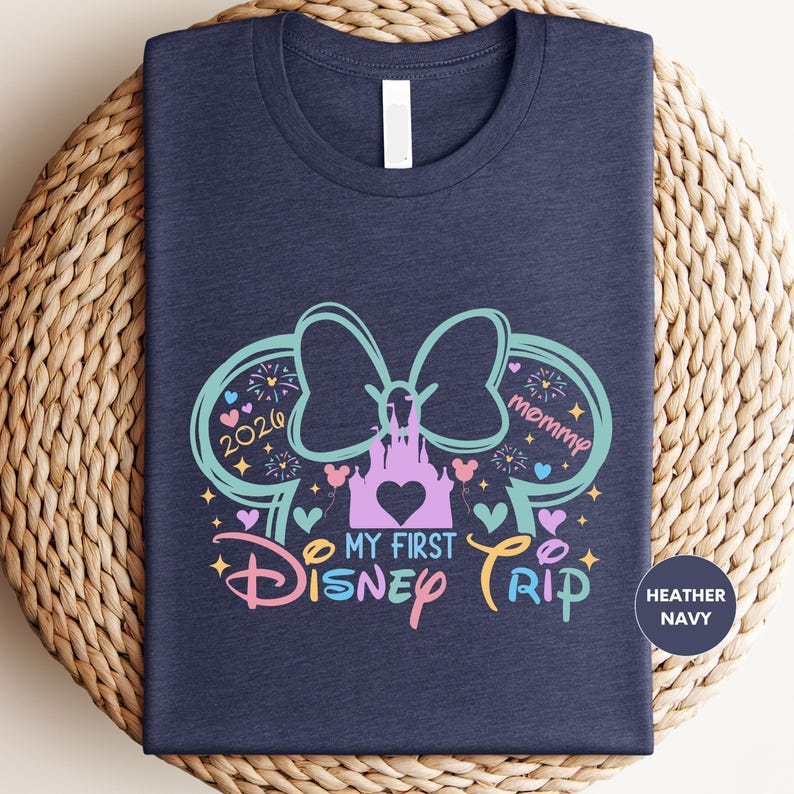A navy blue t-shirt with a colorful graphic design featuring a castle, Mickey Mouse ears, and the text "My first Disney trip" and "2020 Mommy".