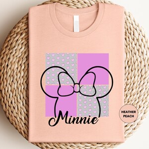 A pink t-shirt with a graphic design featuring a bow and hearts, along with the text "Minnie" below the bow.