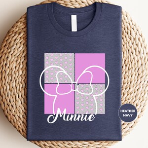 A navy blue t-shirt with a graphic design featuring a pink bow and a pattern of pink hearts on a dark background.
