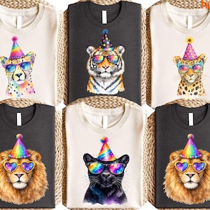 May include: A collection of six t-shirts featuring watercolor illustrations of big cats. Each shirt showcases a different animal, including a cheetah, tiger, leopard, lion, and panther, all wearing party hats and sunglasses with rainbow lenses.