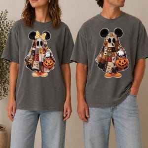 Peut inclure: Deux t-shirts gris anthracite à manches courtes avec un motif de fantôme portant une courtepointe en patchwork et des oreilles de Mickey Mouse. Le fantôme de gauche porte un nœud jaune à pois, et les deux tiennent un seau citrouille rempli de bonbons.
