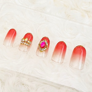 Peut inclure: Cinq pointes d'ongles ombrées avec un dégradé de blanc à rose. Deux pointes présentent des accents de paillettes dorées et des strass, une a un strass rose et deux sont unies.