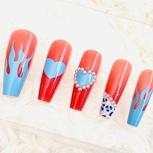 May include: Set of six red press-on nails with different blue designs. One nail has a blue flame design, two nails have a blue heart design, one nail has a blue heart with pearl accents, and one nail has a blue and white leopard print design.